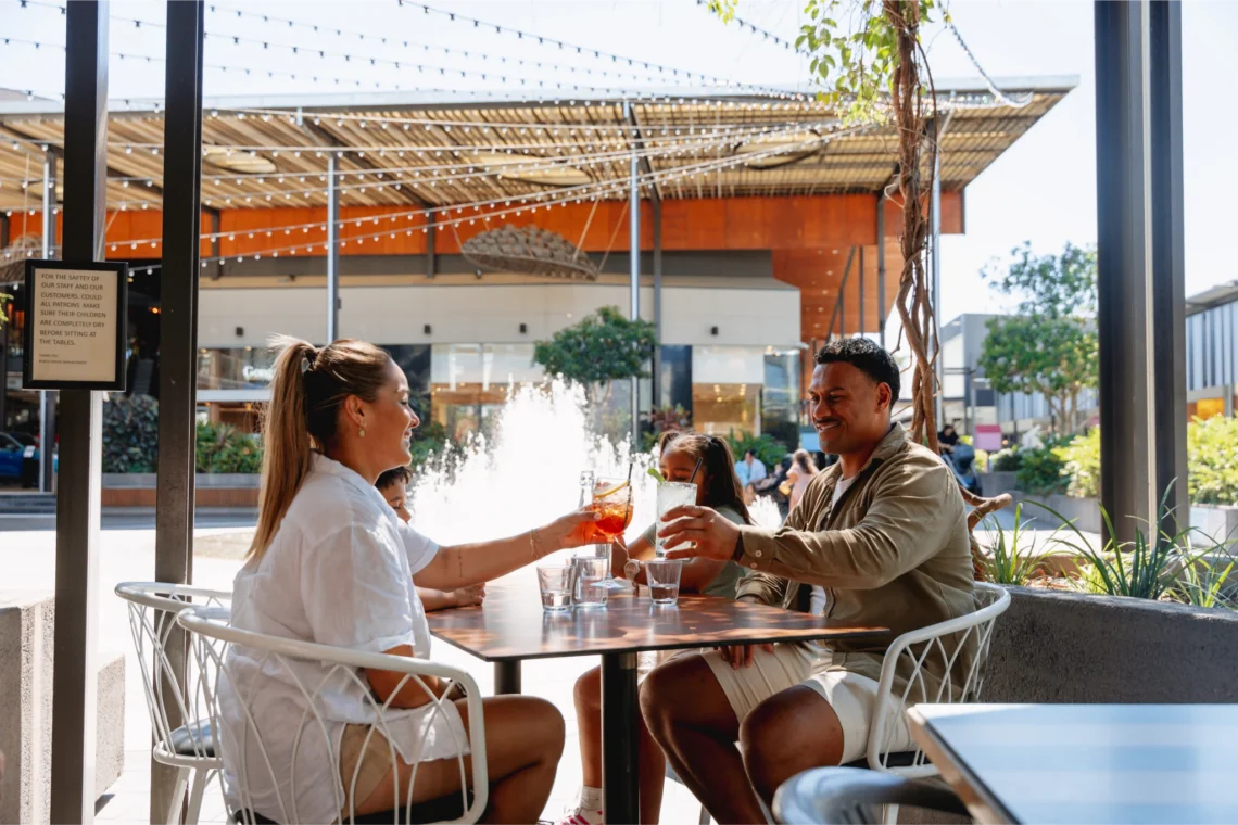 Family toasting drinks at an outdoor cafe table near a fountain